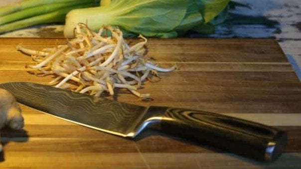 Frische Sojasprossen neben einem japanischen Messer auf einem Schneidebrett