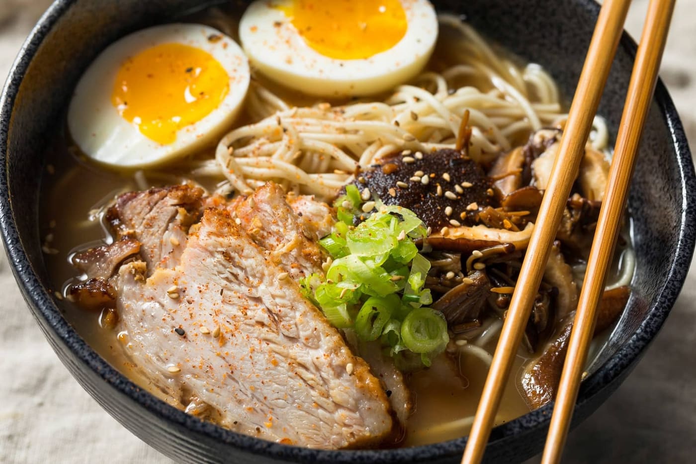 Cremige Tonkotsu-Ramen mit Chashu, Ei, eingelegtem Ingwer und Würz-Toppings am Rand